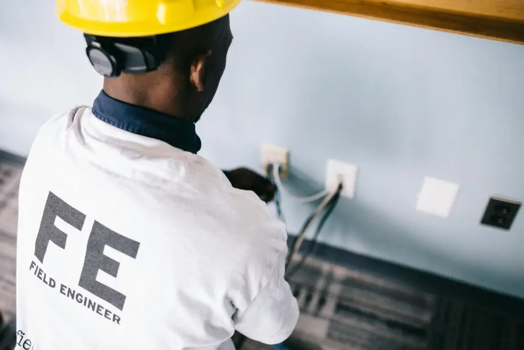 pexels-photo-442160-442160 From above back view unrecognizable black field engineer wearing white shirt and protective hardhat sitting on floor and checking voltage in wall plugs