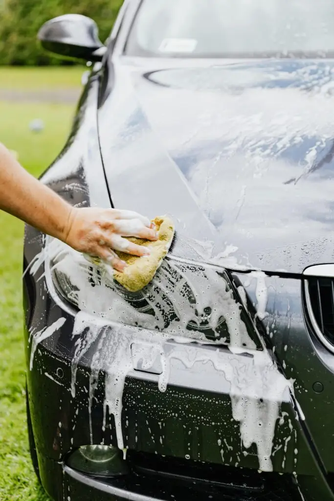 pexels-photo-4870700-4870700 Person washing a black car's headlight with a sponge and soap outdoors.