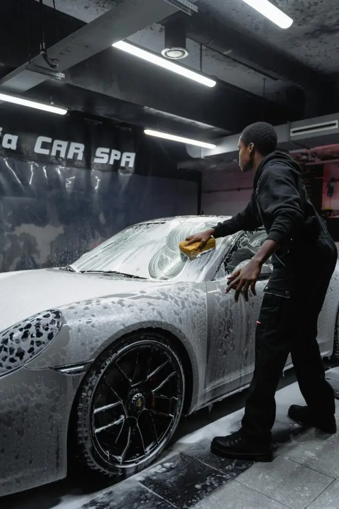 pexels-photo-6873176-6873176 Employee in uniform cleaning a luxury car with foam at an indoor car spa.